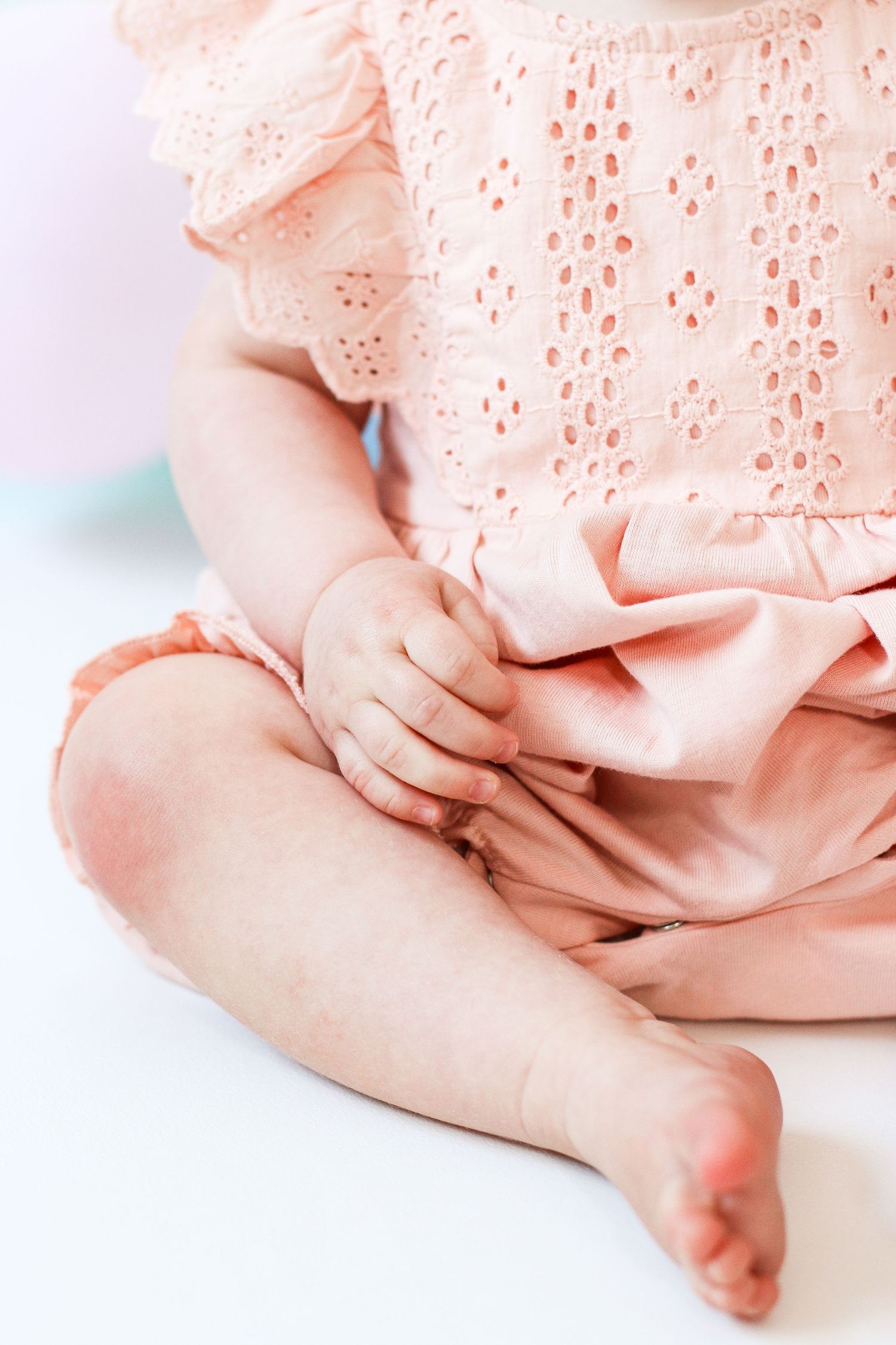 Close-up of baby wearing pink dress showing delicate details of tiny bare feet on white background, during birthday shoot in Nottingham
