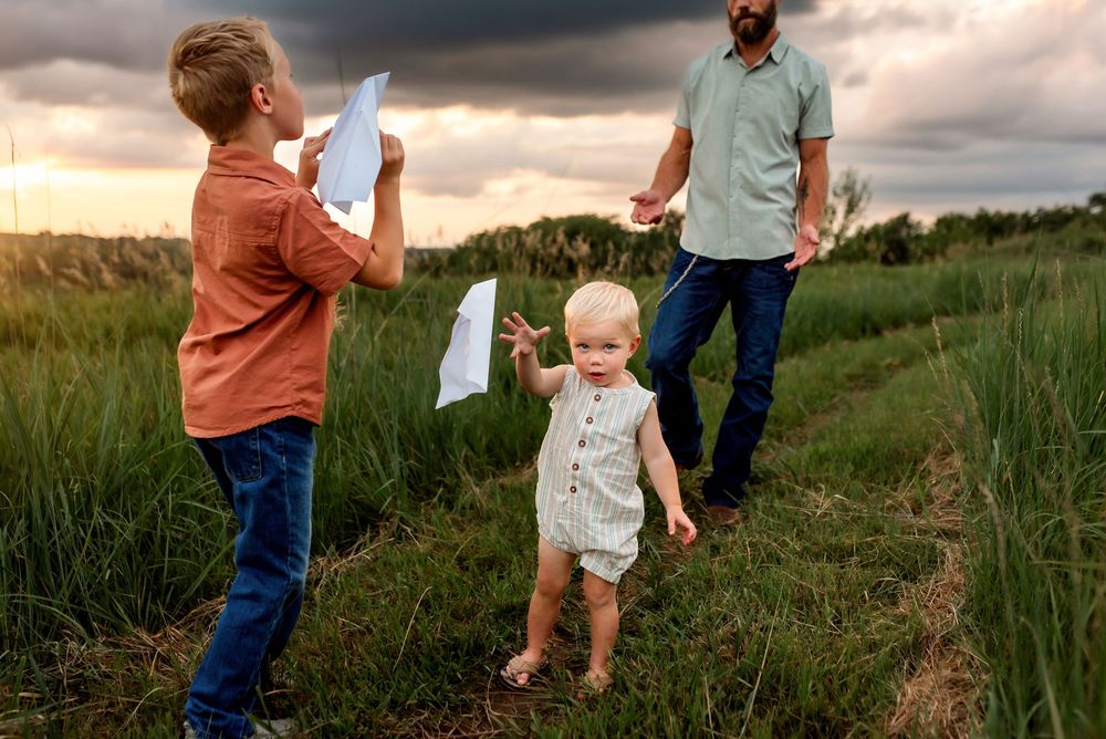 A couple walks through a lush green meadow at sunset while holding a small child between them.
