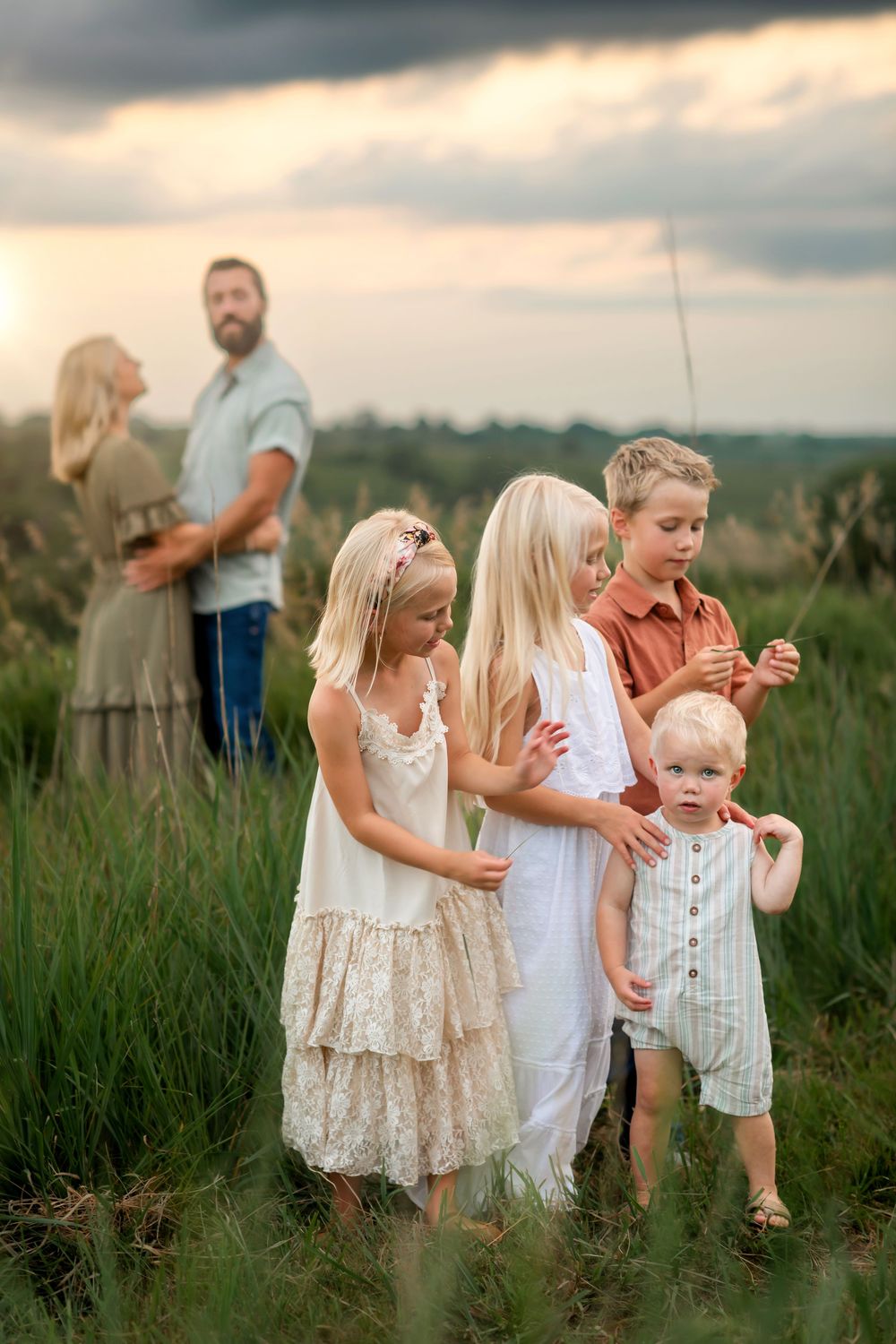 Family enjoys tender moments together in a sun-kissed field of tall grass during golden hour.