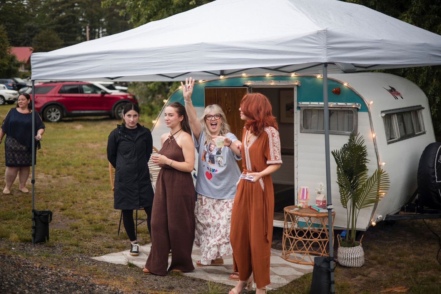 A group of people gathered under white canopy tents at an outdoor event on a grassy field.
