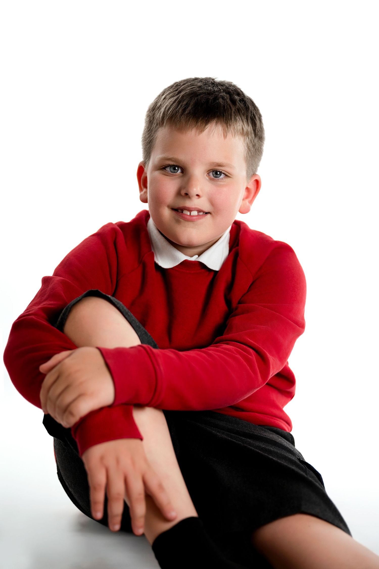 Child wearing red sweater and black pants poses casually on white background in three similar portraits.