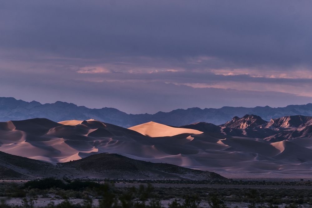 Desert sand dunes bathed in purple twilight with mountain silhouettes in Death Valley.