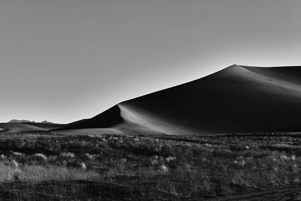 Black and white lone sand dune rising above sparse desert scrubland at dusk.