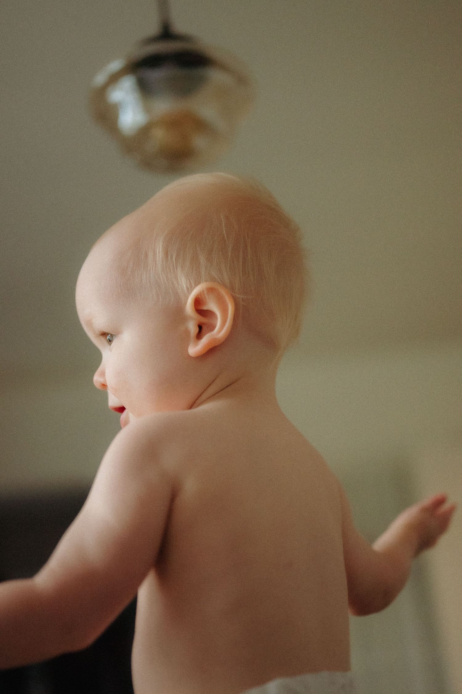 Side view of an infant with bare skin shown from shoulders up against a soft blurred background.