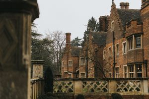Gothic brick mansion with ornate balustrade and tall chimneys photographed against moody winter sky.
