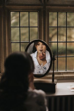A moody reflection in a vintage mirror shows a silhouette against a window with raindrops on a cloudy day.