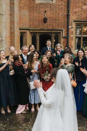 A joyful wedding scene outside a brick building with a group laughing together as a bride in white stands before them.
