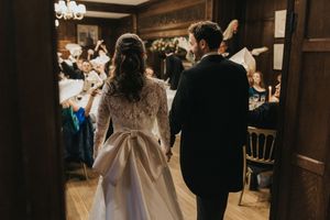 A couple in formal wedding attire stands close together in an intimate, dimly lit indoor setting.