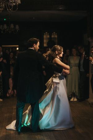 A couple shares their first dance as newlyweds on a dark wooden dance floor with a romantic blue glow beneath them.