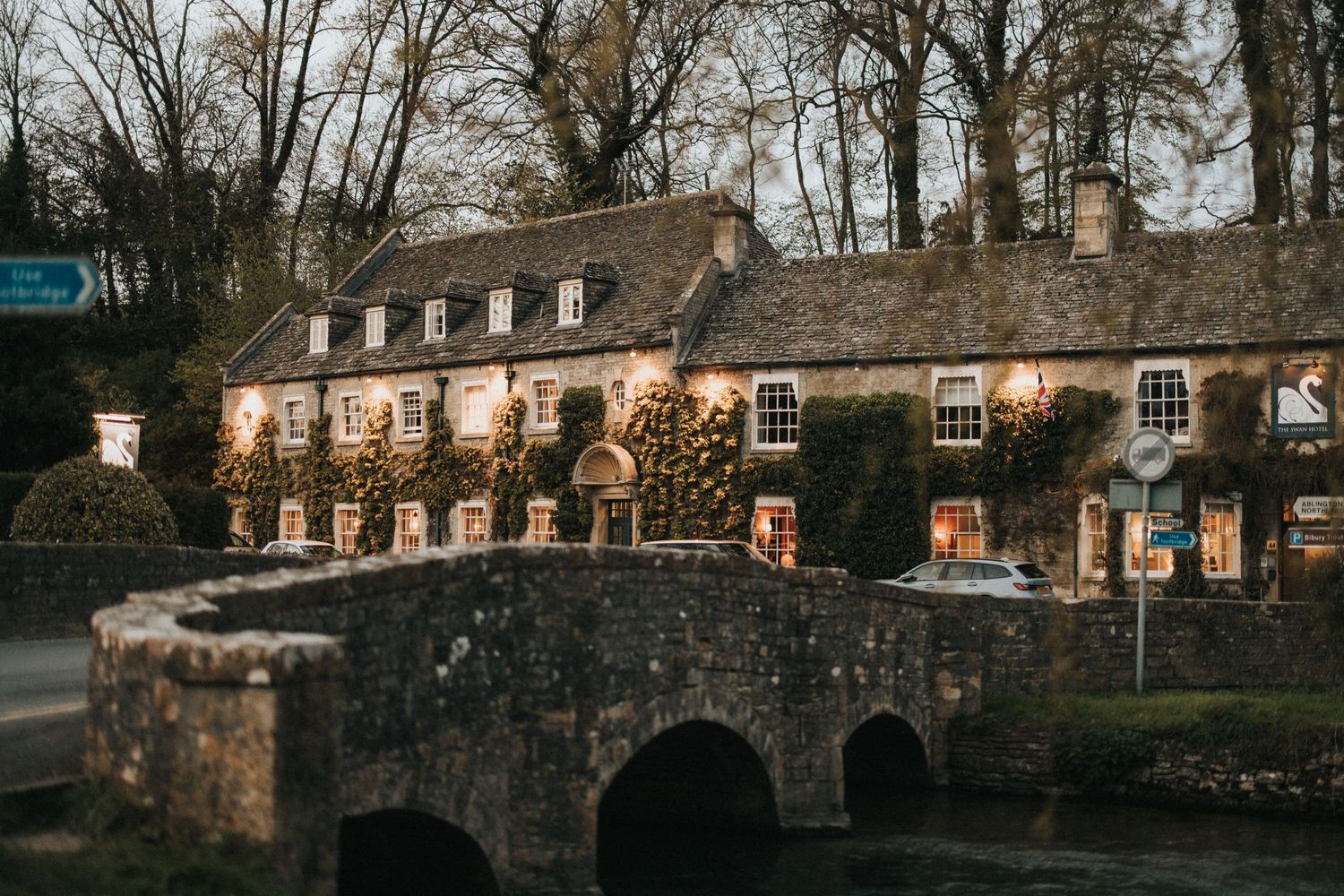 A panoramic view of historic stone buildings and a bridge along a rustic countryside setting at dusk.