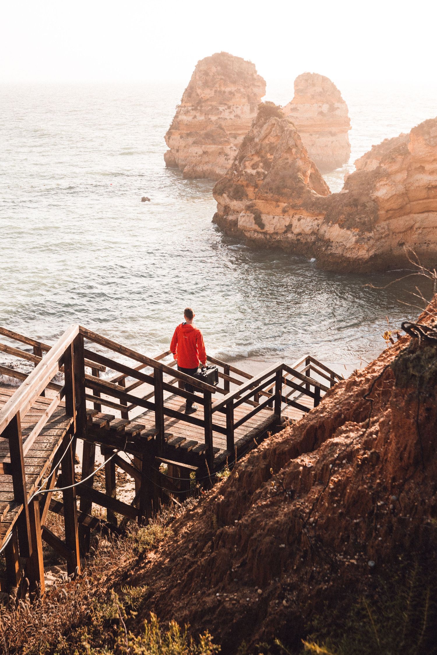 Black hardshell case sits open on rocky coastline with red cliffs and ocean waves in the background.
