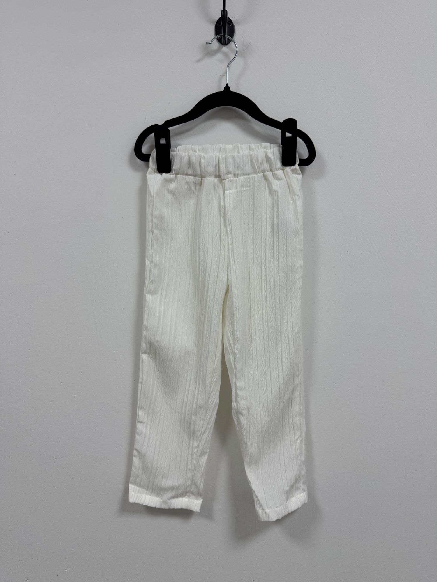 White linen pants with elastic waistband hanging on black clothes hanger against light gray background.