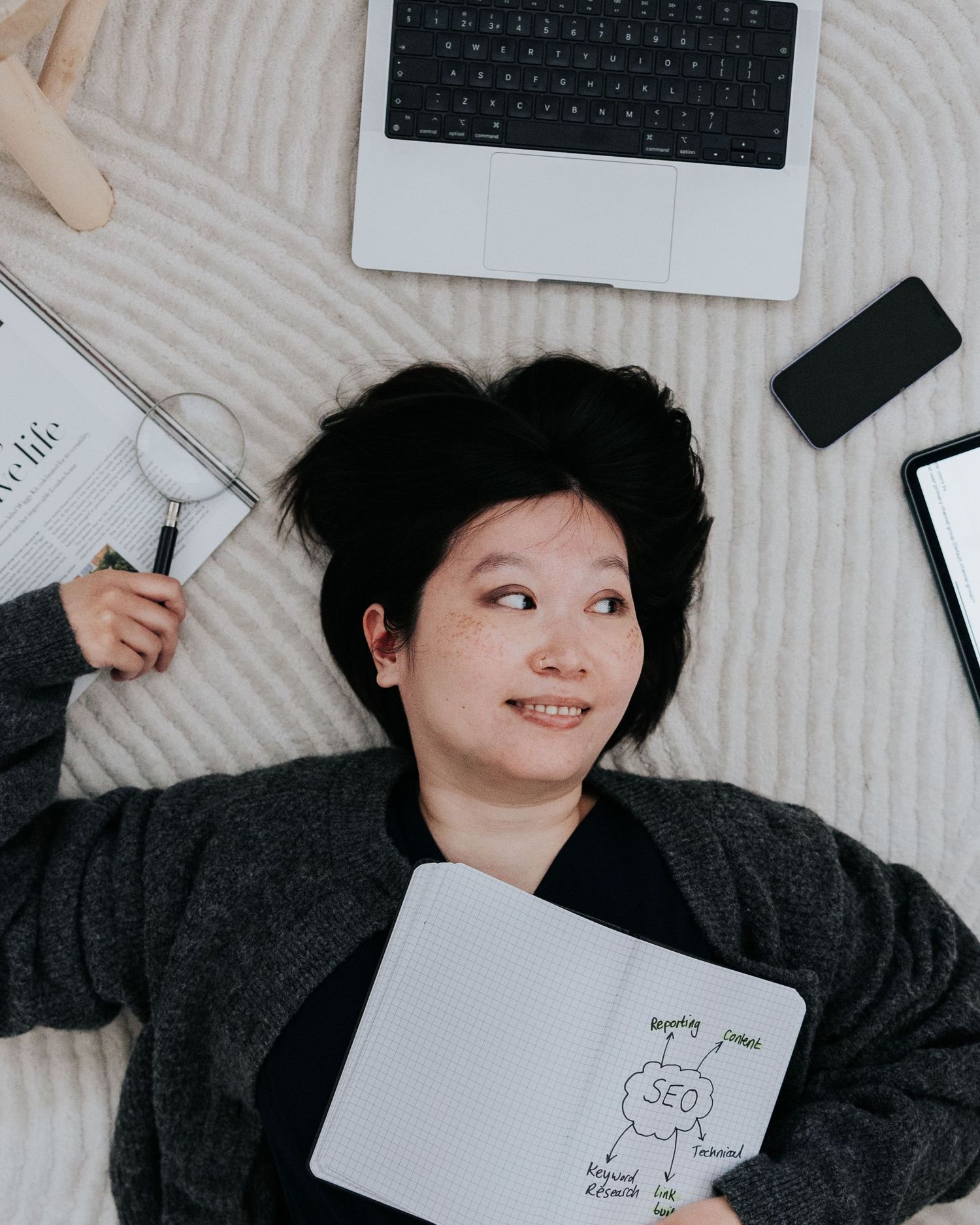 Person lying on white bedding with laptop, phone, and notebook featuring a simple stick figure drawing.