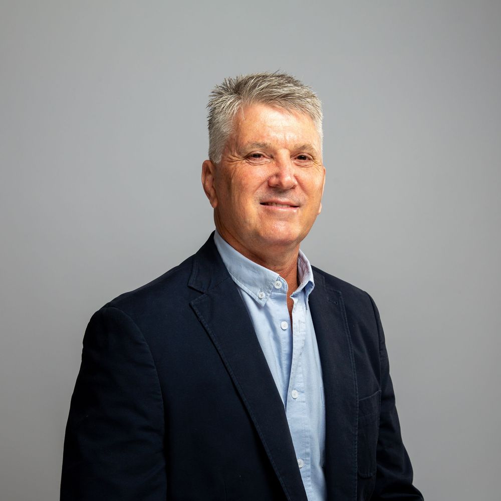 Professional business headshot showing someone in a dark blazer and blue collared shirt against a neutral background.