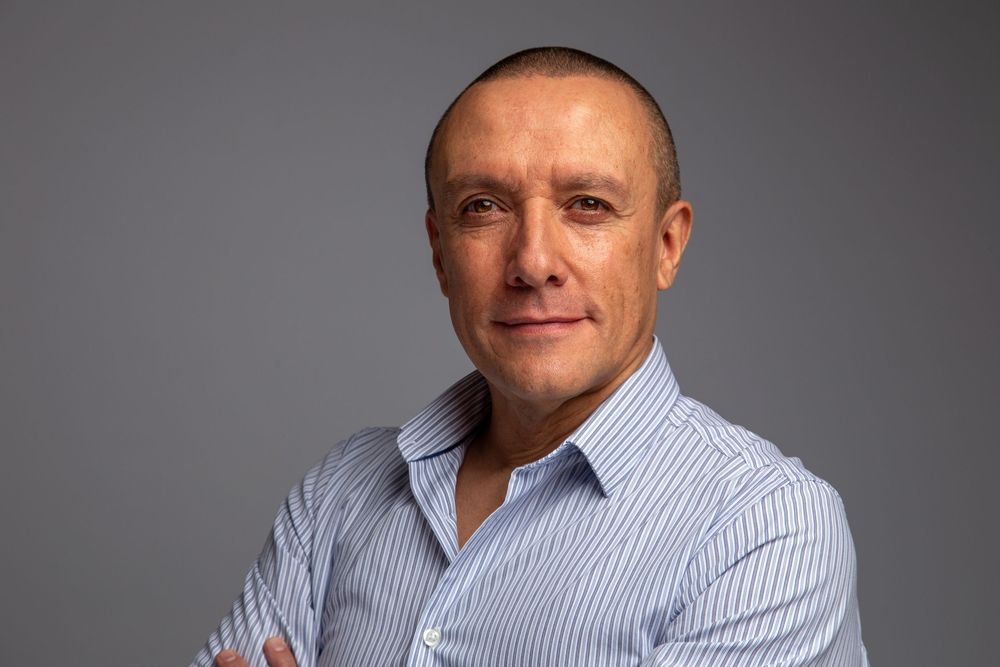 A collage of four professional headshots showing someone in a light blue button-down shirt against a grey background.