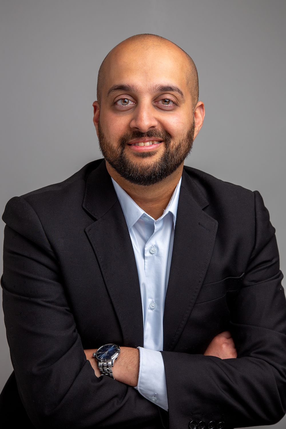 Professional corporate headshots of person in black suit and light blue shirt against gray backdrop in different poses.