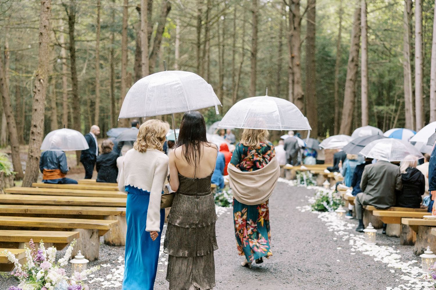 An outdoor winter wedding ceremony arranged in a snowy forest with wooden benches set up for guests and decorative details.