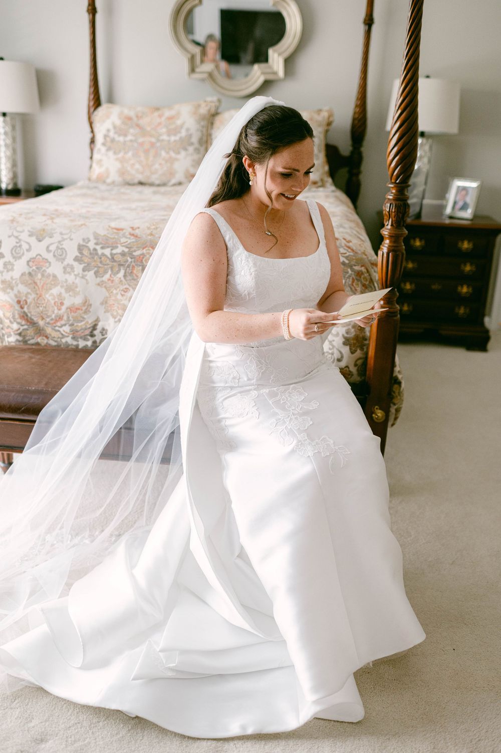 An elegant white wedding gown with a flowing veil in a bedroom setting.
