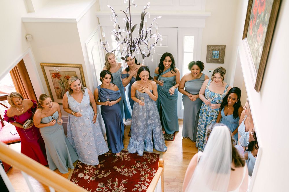Bridesmaids in blue and floral dresses gathered on an elegant staircase.