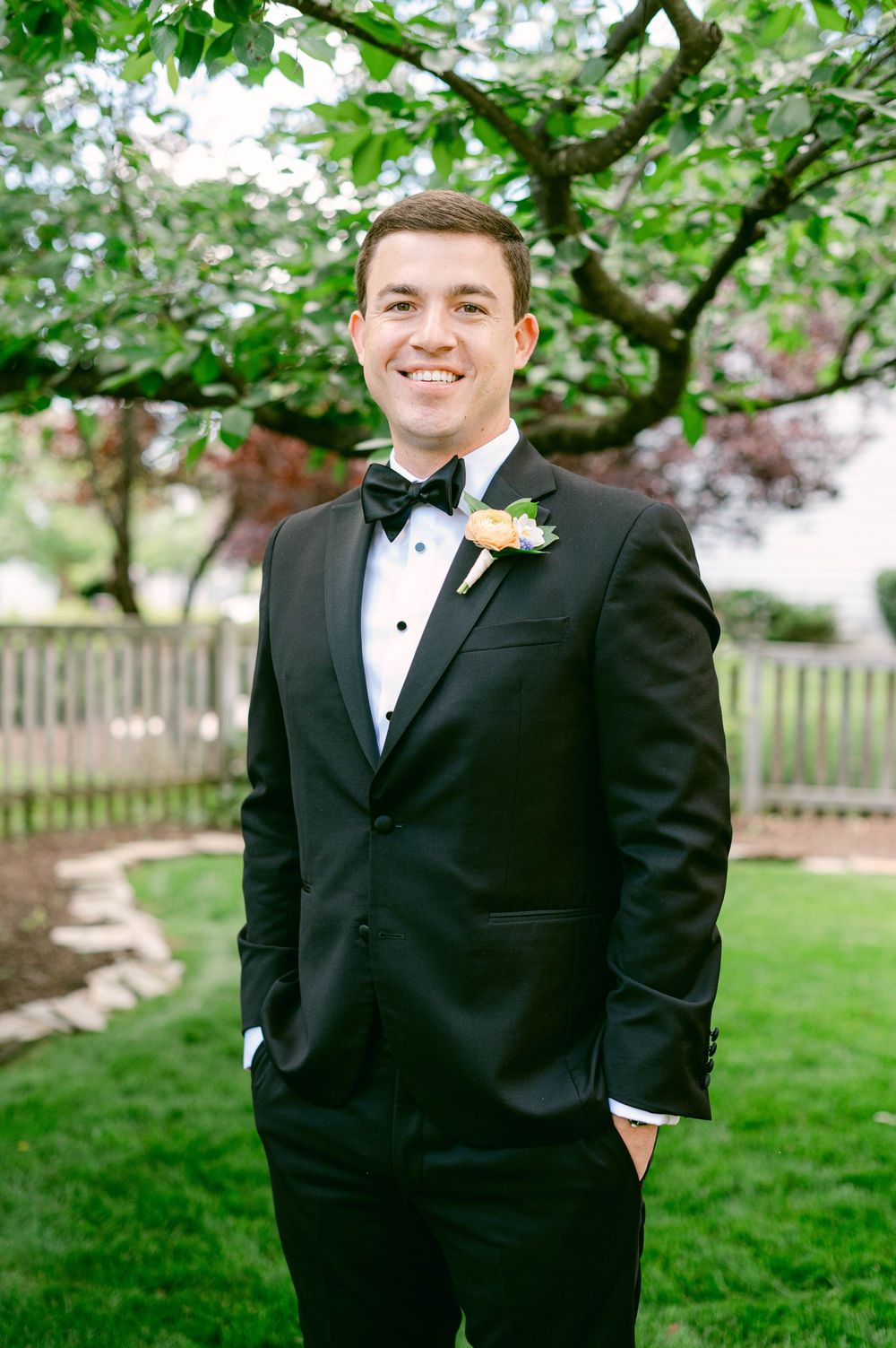 Formal portrait in garden setting showing classic black tuxedo with boutonniere.