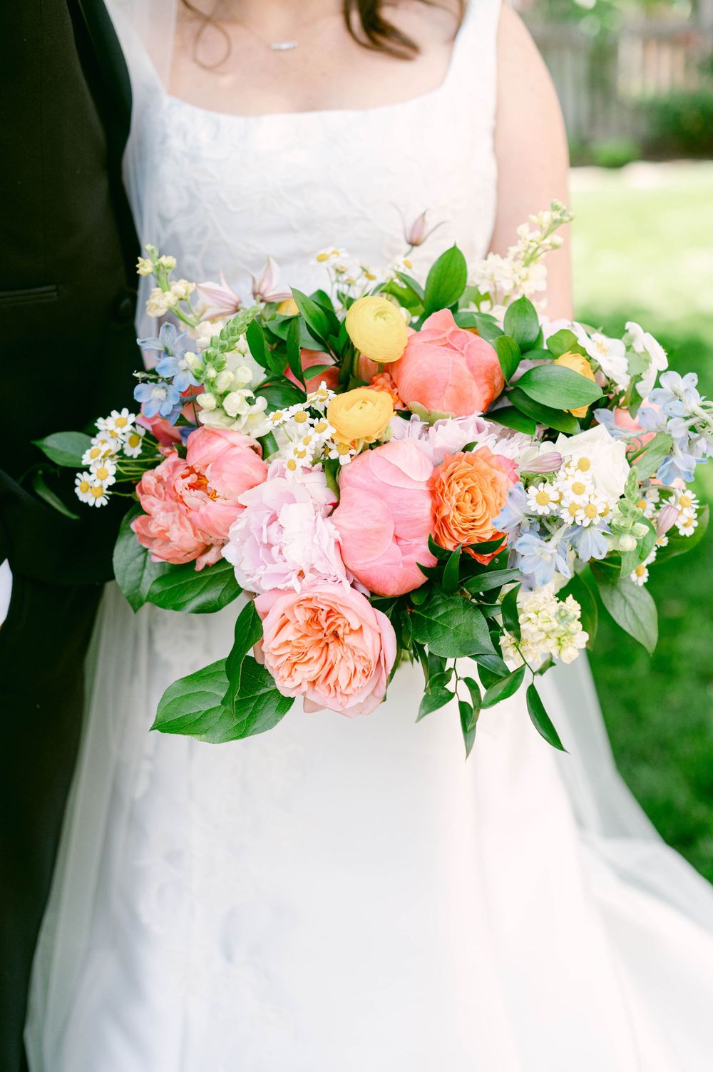 A lush spring wedding bouquet with coral peonies, roses and mixed seasonal flowers.