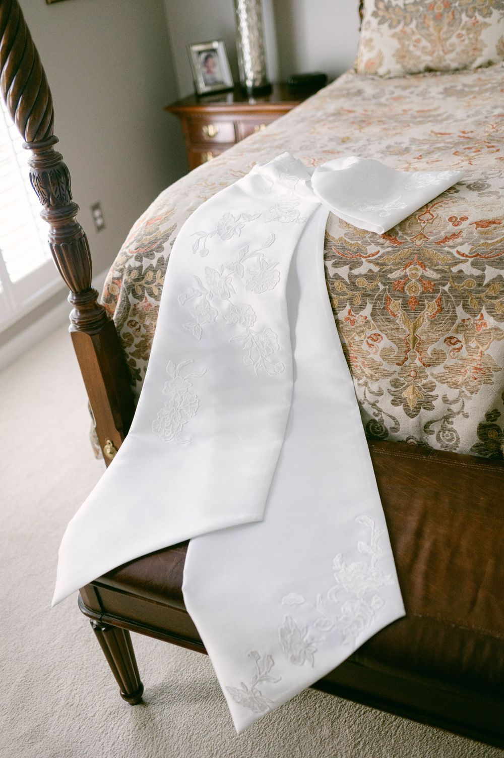 White wedding dress with intricate lace detail draped over wooden bedroom furniture.