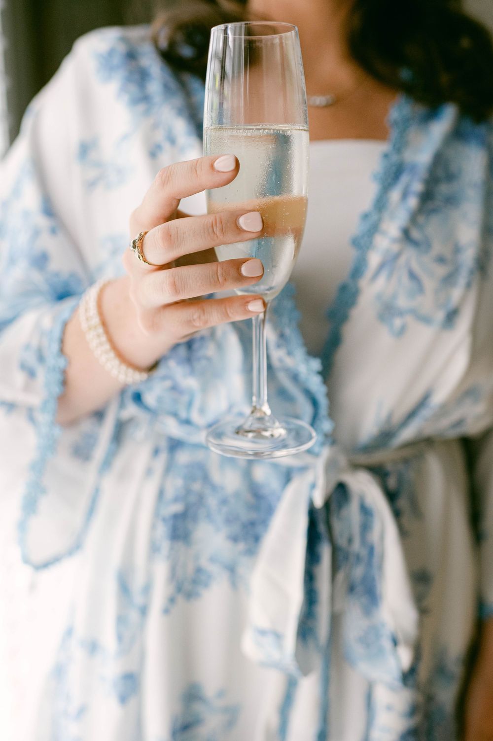Close-up shots of hands holding champagne glasses in blue and white floral robes.
