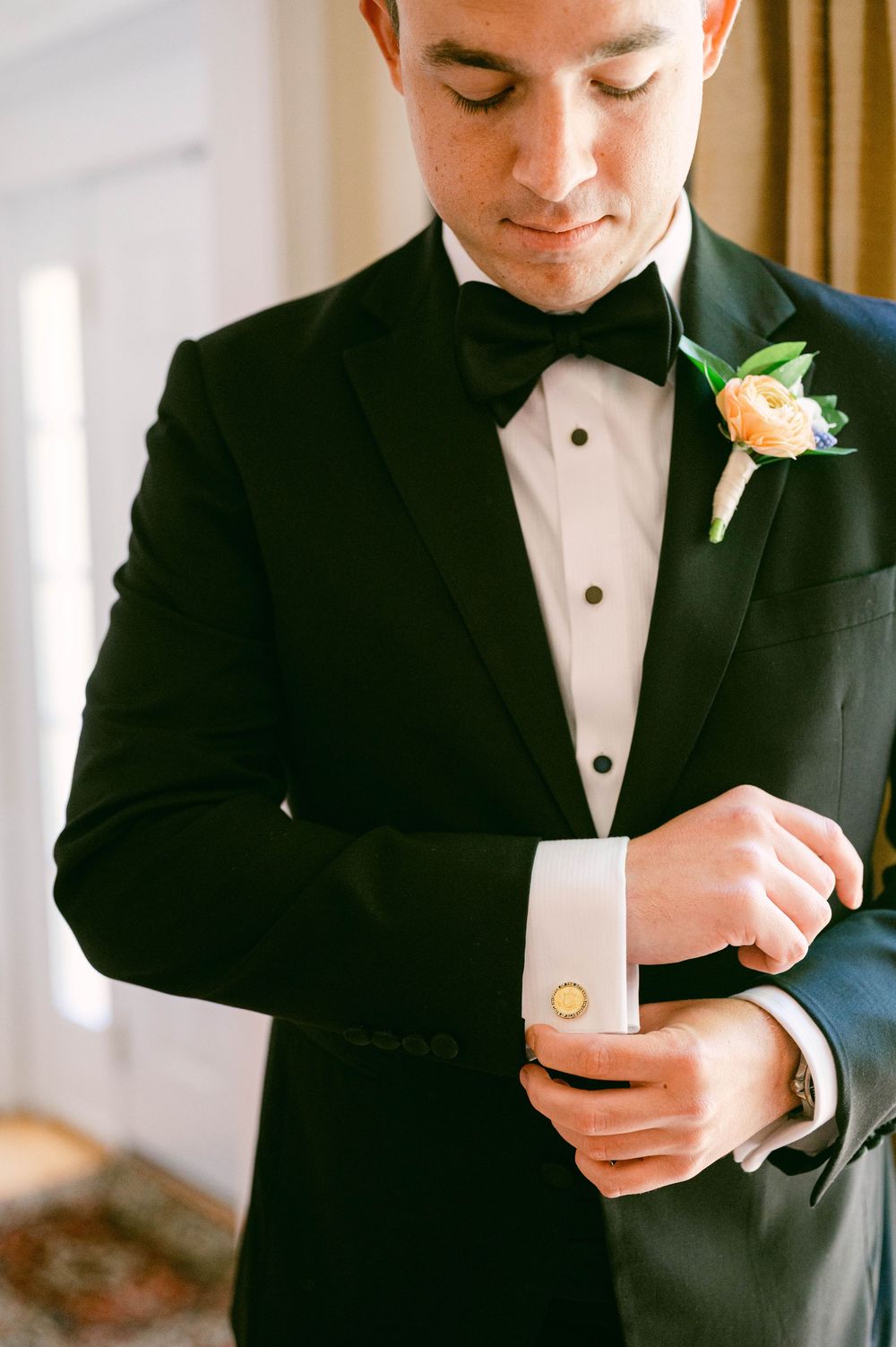 Detail shots of groom adjusting cufflinks while wearing classic black tuxedo.