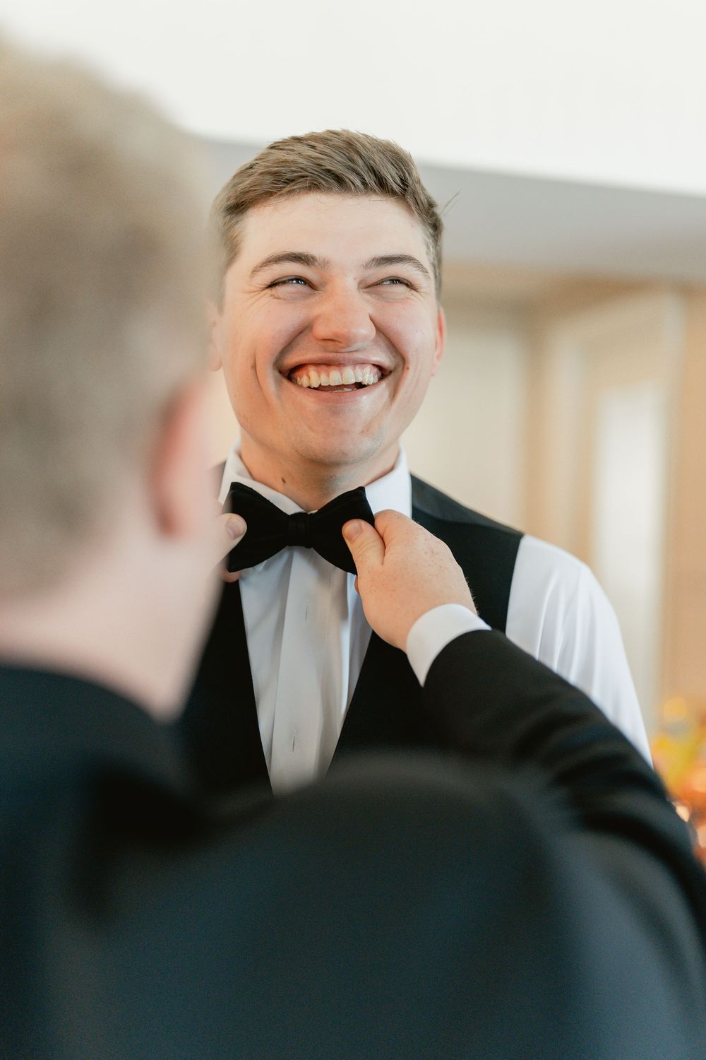 A sequence of candid laughter expressions in black and white formal attire at what appears to be a wedding event.