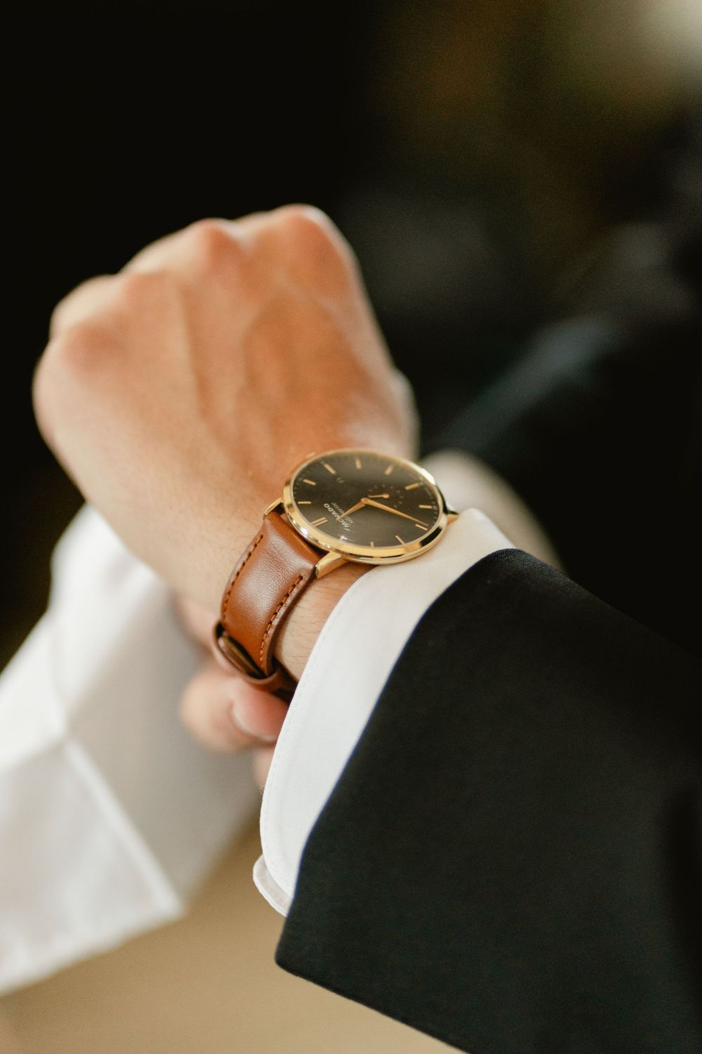 Close-up of hands with a gold watch and formal attire adjusting sleeves during wedding preparation.