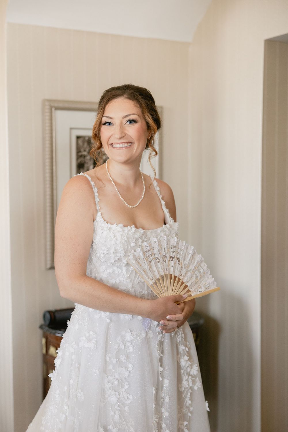 A bride in an elegant lace wedding dress poses with a decorative hand fan.