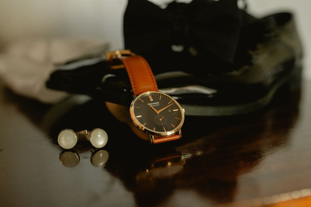 Elegant watch with brown leather strap and cufflinks on reflective dark surface.