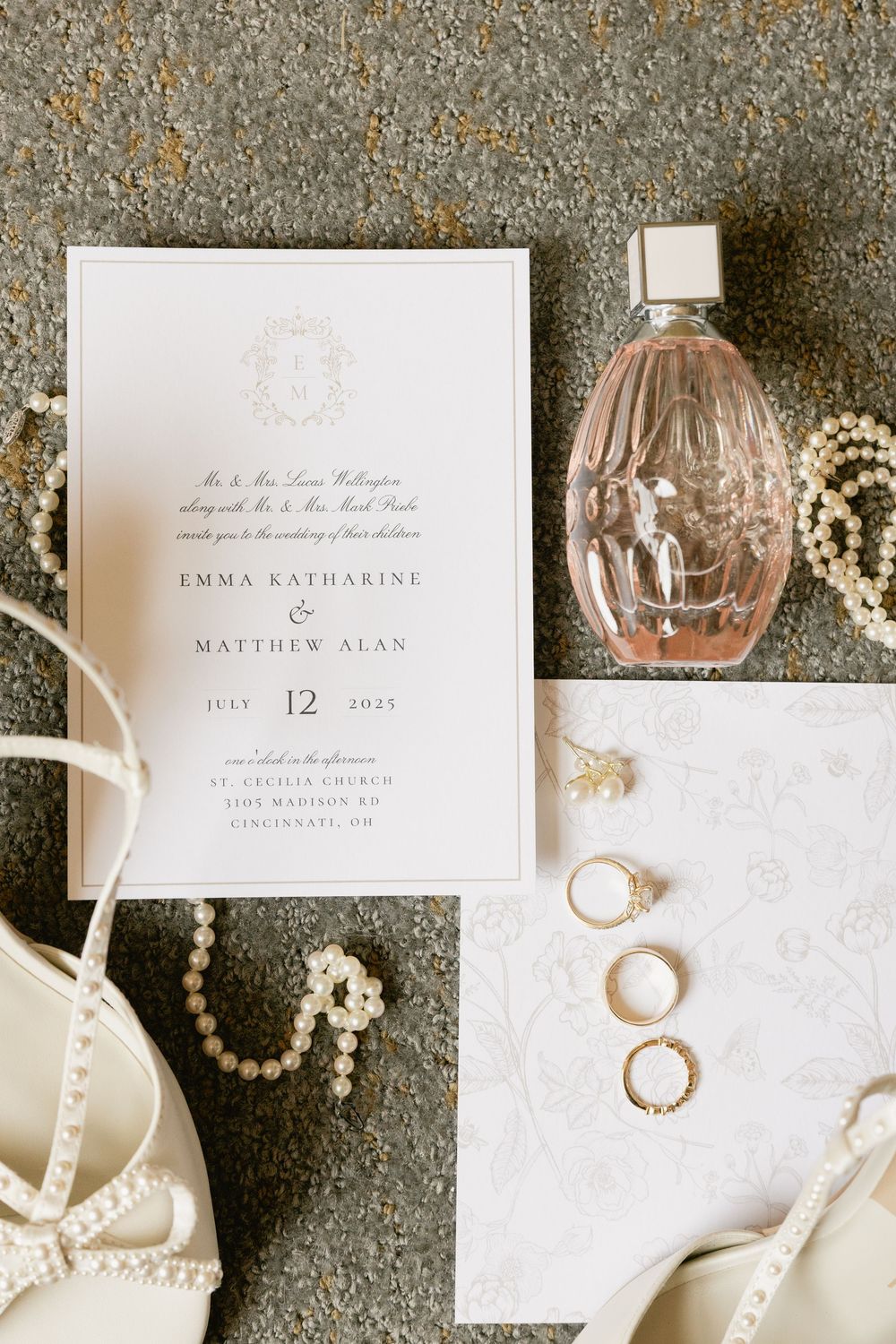 Wedding invitation details with perfume bottle, pearl necklace, rings and elegant accessories on gray background.
