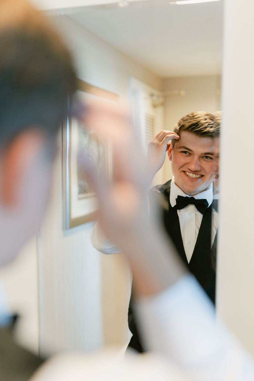 A mirror reflection shows a groom adjusting his bowtie while getting ready.