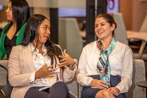 Two professionals in business attire engage in animated conversation during a conference or meeting.