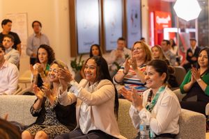 A diverse crowd cheers and applauds during an indoor event.