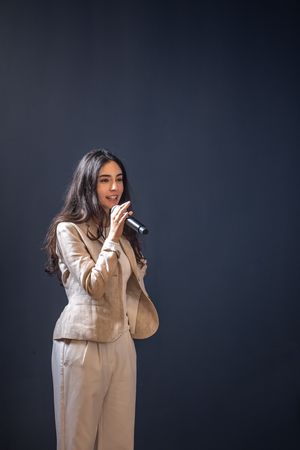 A person in a beige coat performs under dramatic lighting against a dark background in a multiple exposure portrait.
