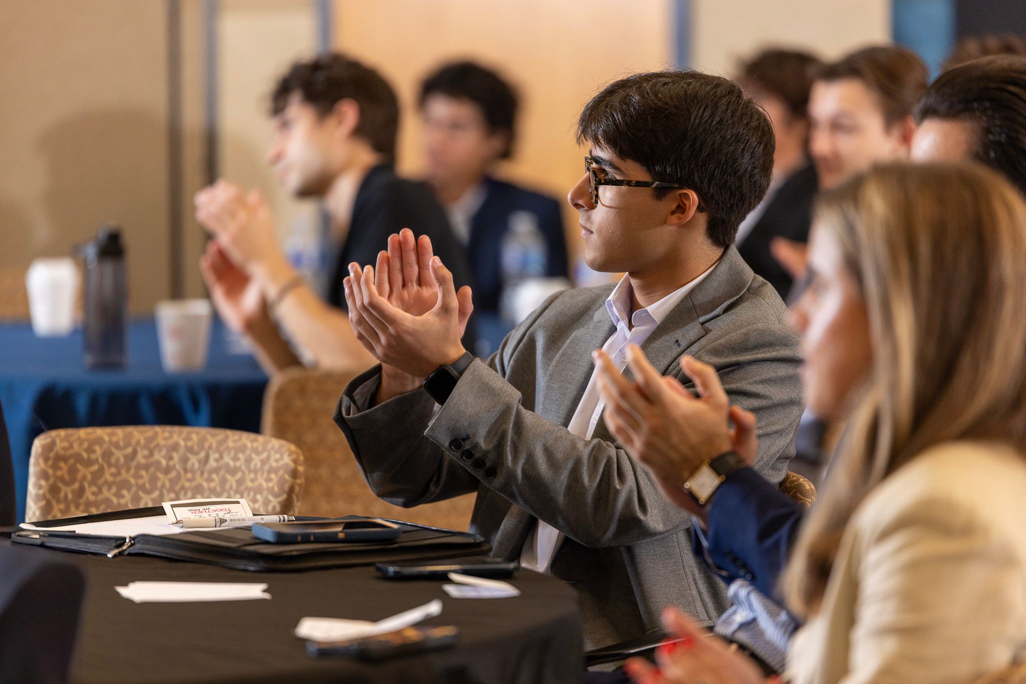 Business professionals seated at a conference table during a meeting applaud and engage in discussion.