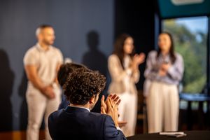 Photographer seen from behind taking photos of people standing on stage during an indoor event.
