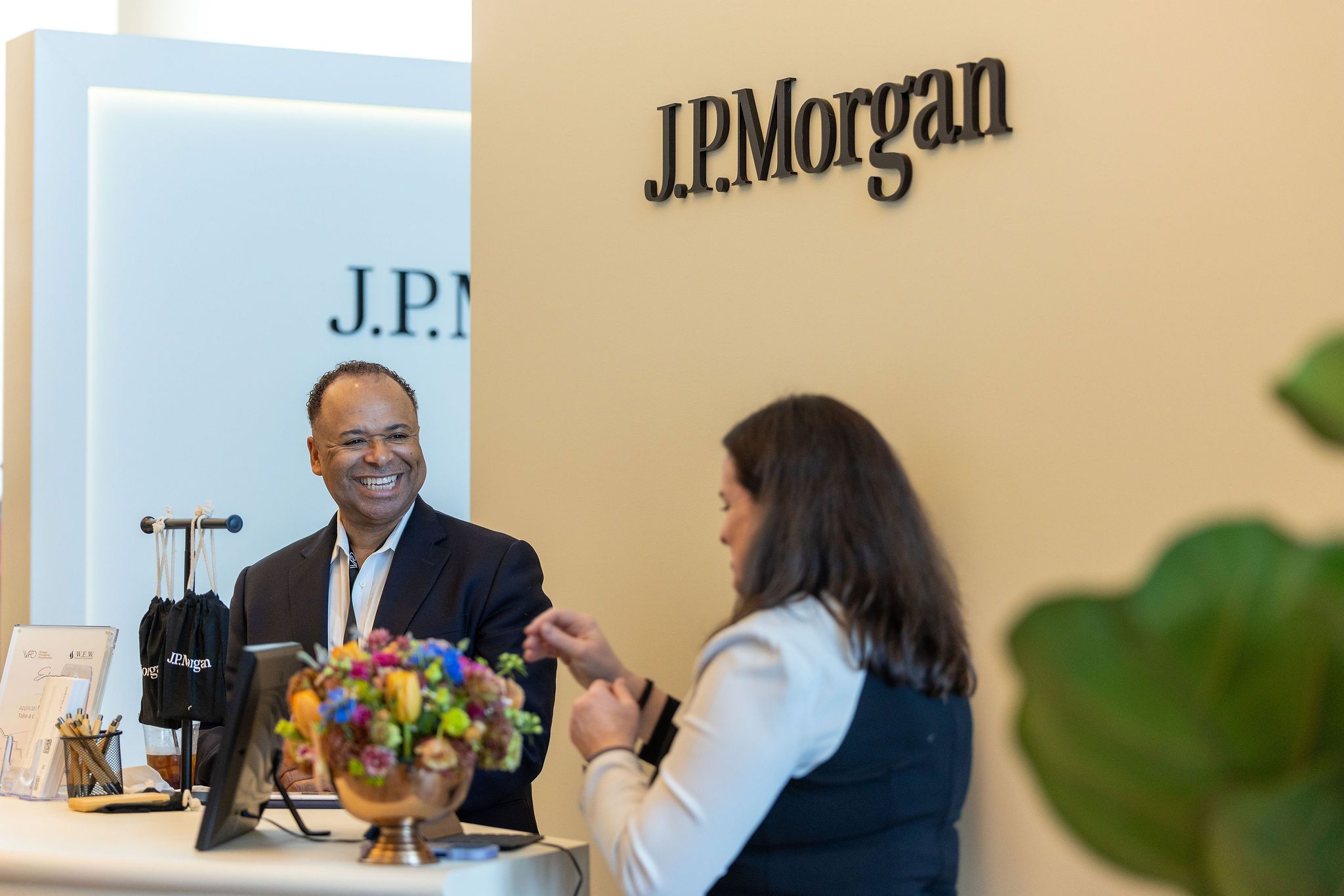 Two professionals smile at a J.P. Morgan branded reception desk in a modern office setting.