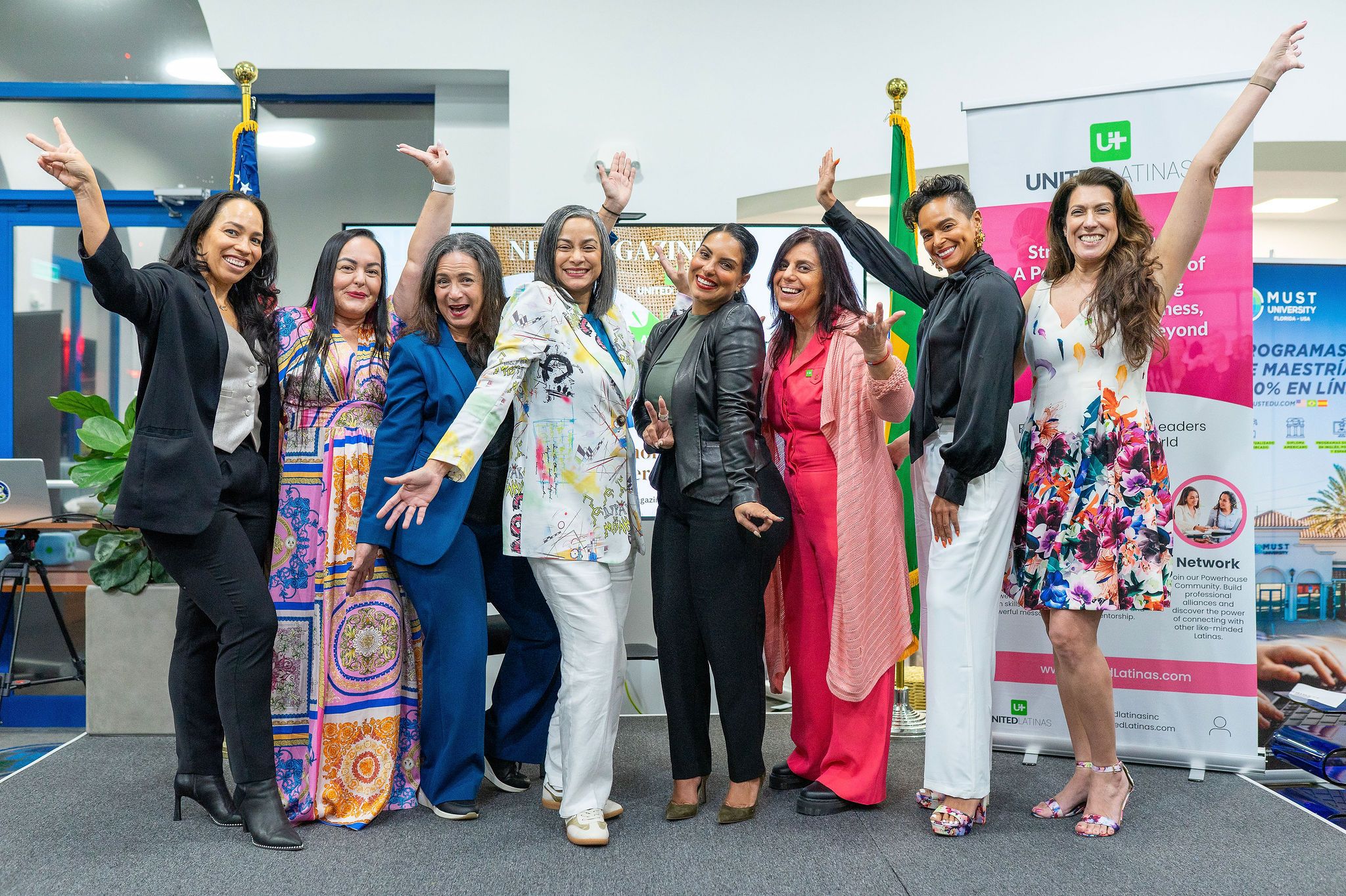 Diverse group of women celebrating together at a professional event, posing joyfully in front of colorful banners.