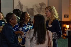 Group of women smiling and conversing at a professional networking event indoors.