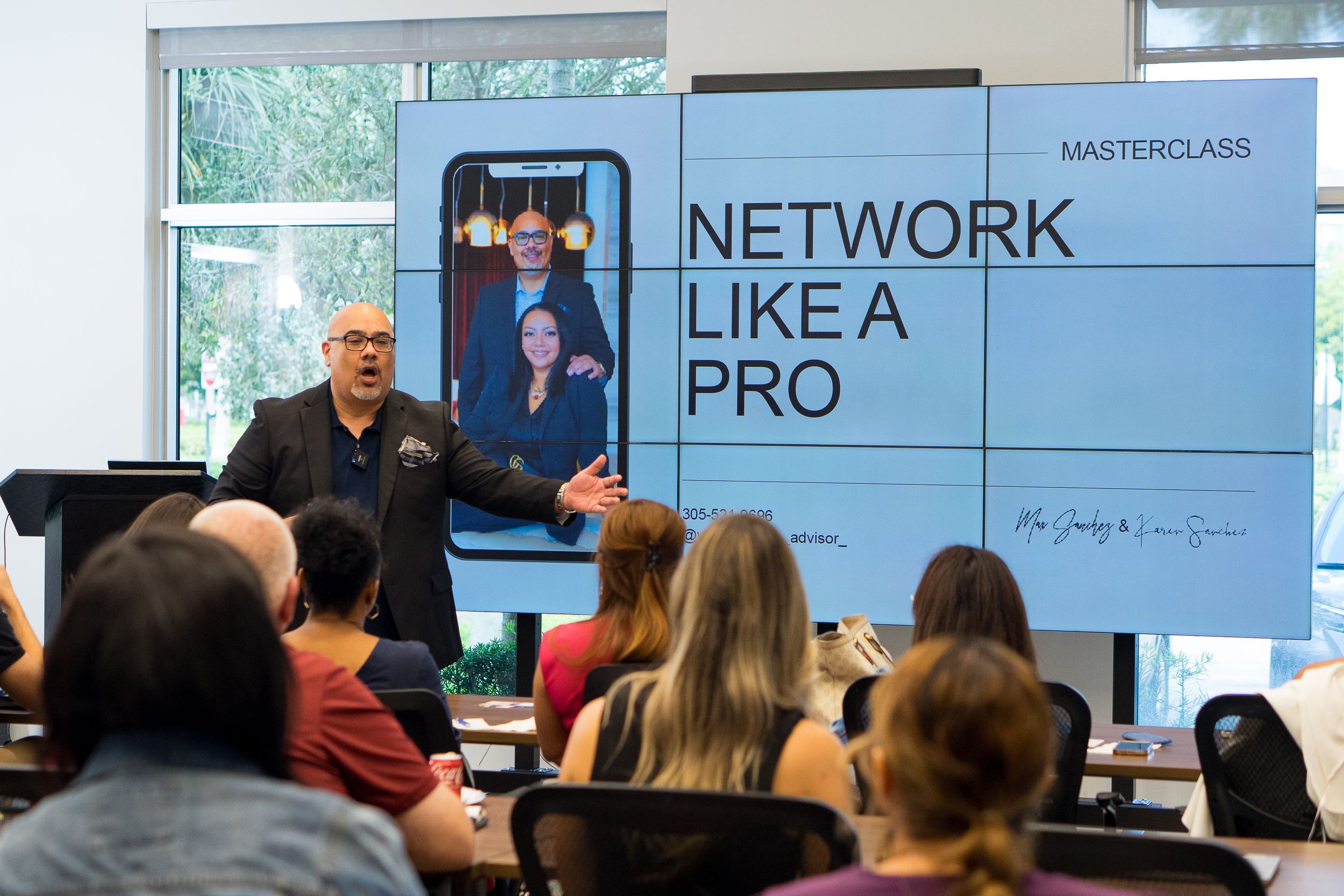 A business presentation takes place in a modern conference room with attendees seated and viewing projected slides.