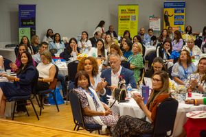 A crowd of attendees sits in rows at a professional conference or workshop in a brightly lit meeting room.