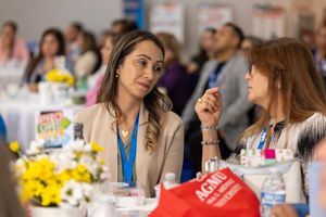 Two attendees having a conversation at a business conference with yellow flowers and refreshments visible on the table.