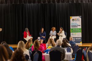 Panel discussion event with speakers seated on stage and audience members watching from chairs at a business conference.