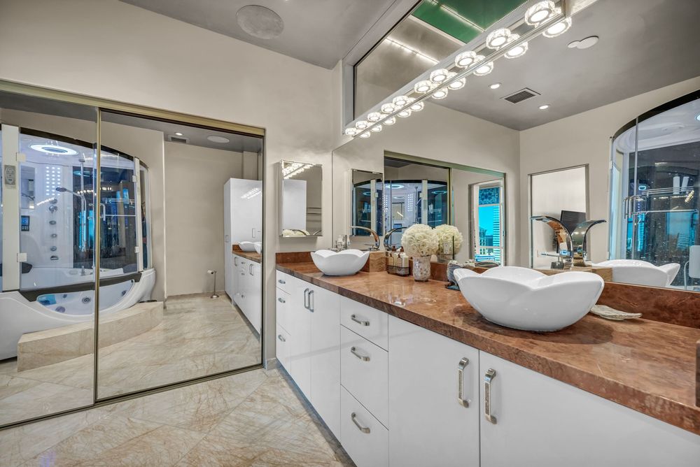 Spacious modern bathroom with dual vessel sinks, white cabinetry, and large mirrors with bright lighting.