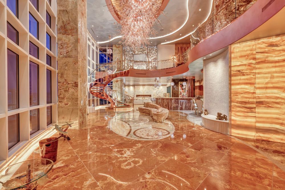 Grand luxury penthouse lobby with soaring ceilings, marble floors, crystal chandelier, and spiral staircase.