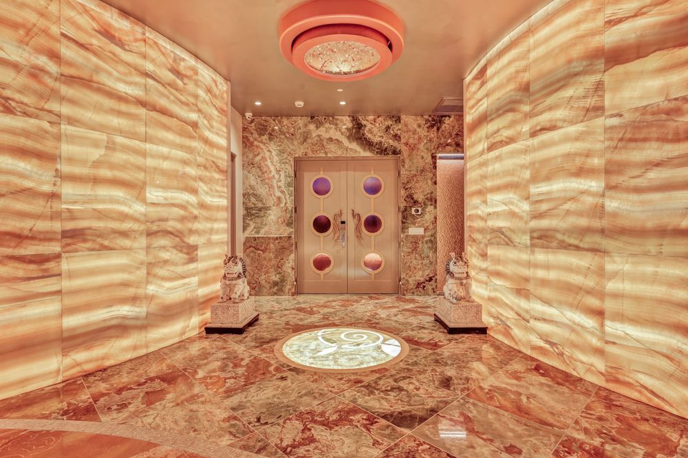 Opulent marble-clad foyer with backlit onyx walls, ornate flooring medallion, and warm ambient lighting.