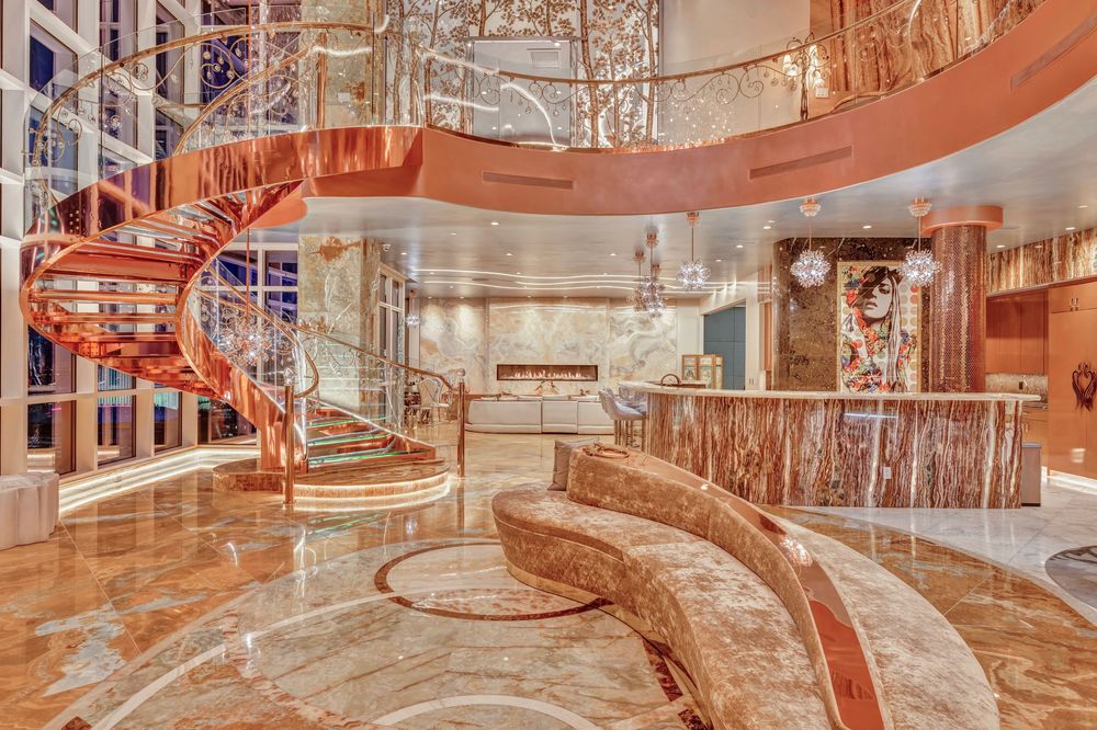Luxurious hotel lobby featuring a rose gold spiral staircase, marble floors, and elegant curved sofa.